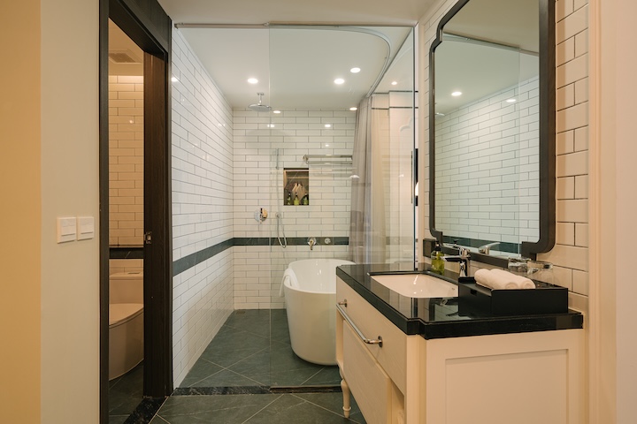Phòng tắm với bồn tắm nằm trắng sau vách kính, gương lớn và bàn lavabo mặt đá tại Soc Village