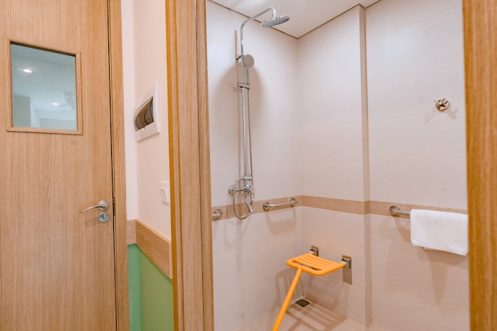 Khu vực tắm đứng trang bị sen cây, tay vịn inox và ghế ngồi gập màu cam trợ giúp