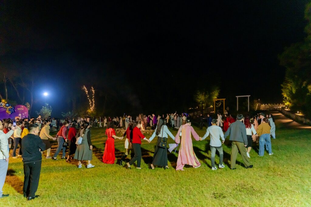 Nhóm khách nắm tay tham gia hoạt động gắn kết ngoài trời trên bãi cỏ tại Sóc Village